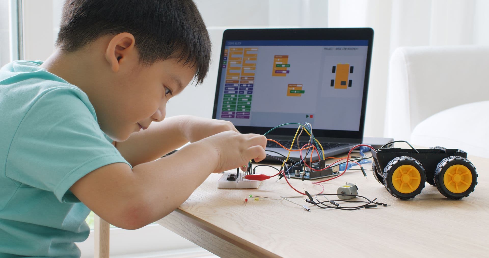 A child coding on a laptop next to a small robot car