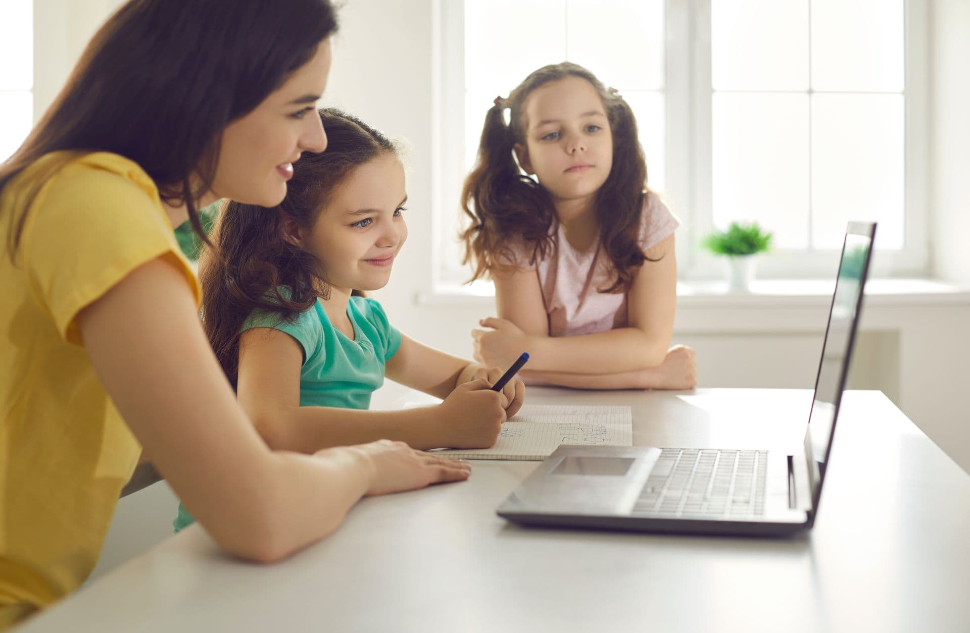 An adult and two children at a table with a laptop