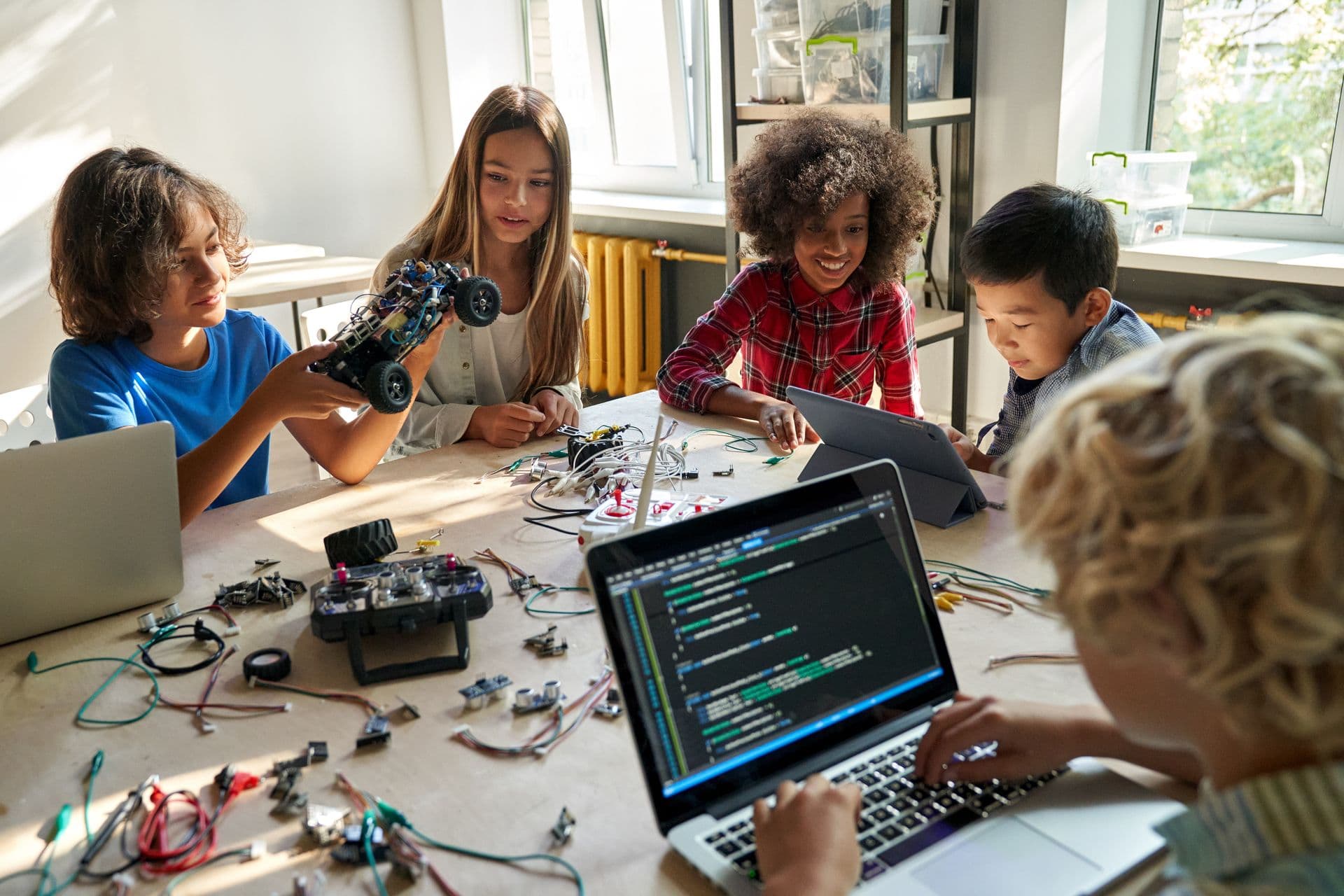 Children working with laptops and robot parts around a table