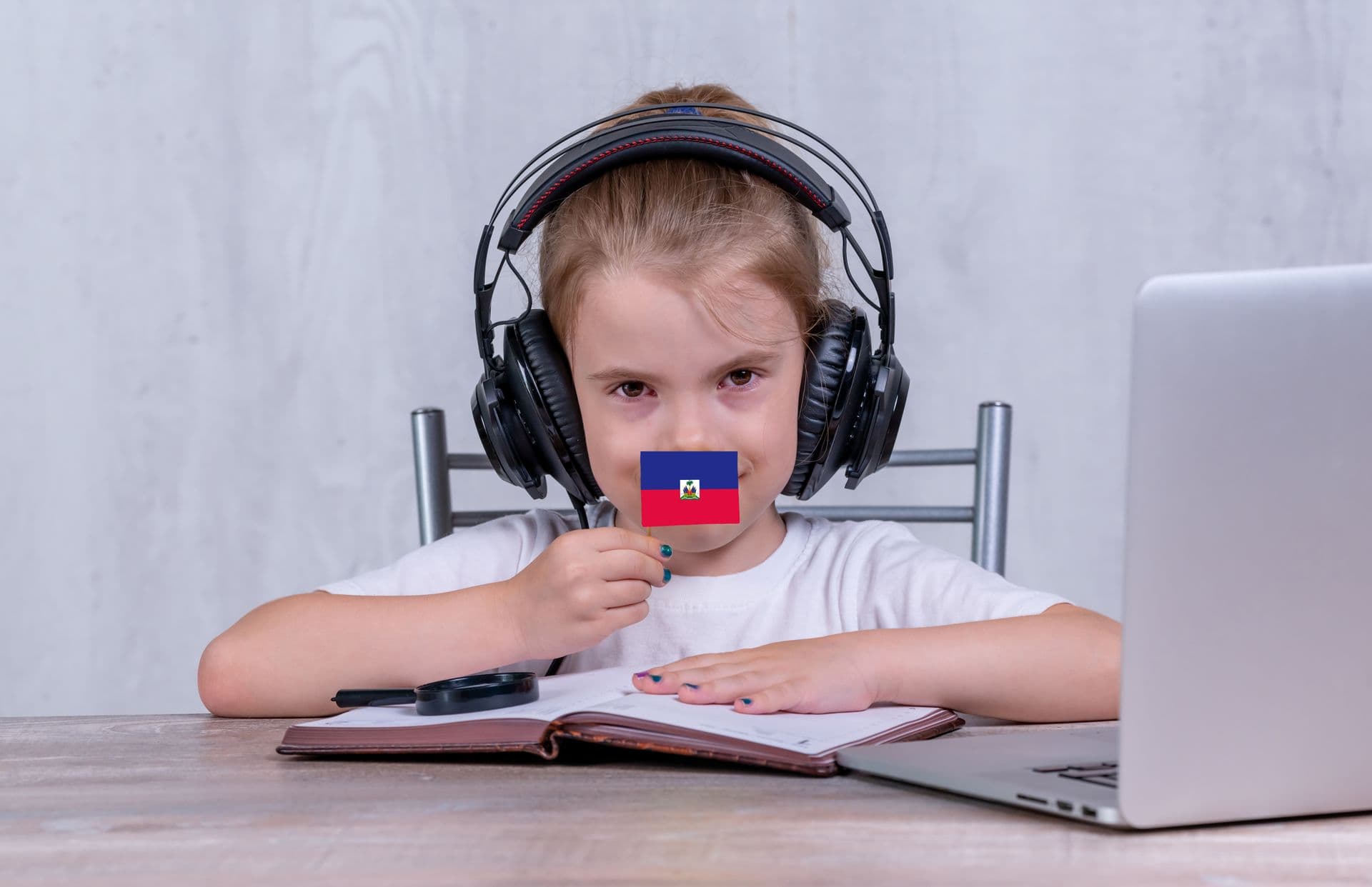 A child wearing headphones at a laptop, holding a small flag