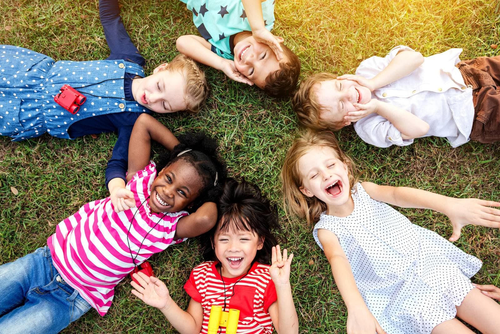 Children lying on the grass and laughing together outdoors on a sunny day